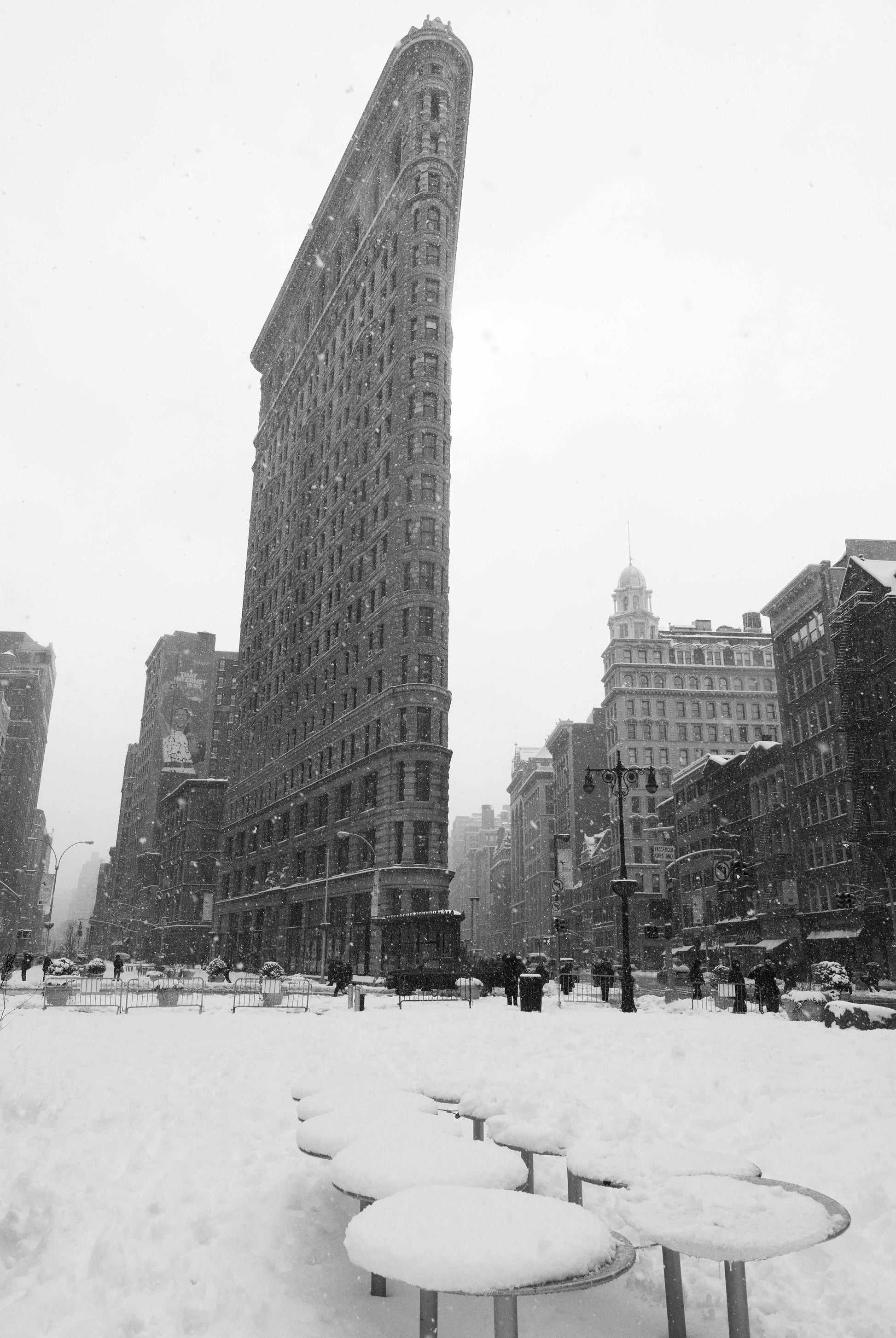 Alessandra Mattanza | FROM A DISTANCE, Flatiron Building. The iconic Flatiron Building stands in a New York winter scene.  Available as a black and white photographic print on clear acrylic.